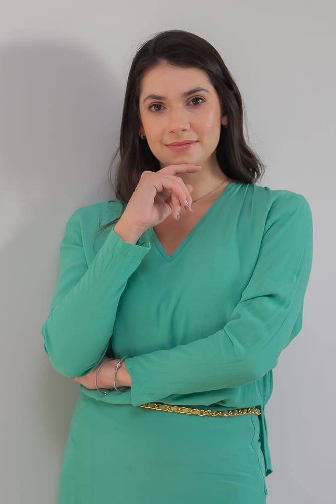 Dra. Carla Eid Gobbi de blusa verde, com a mão apoiada no queixo